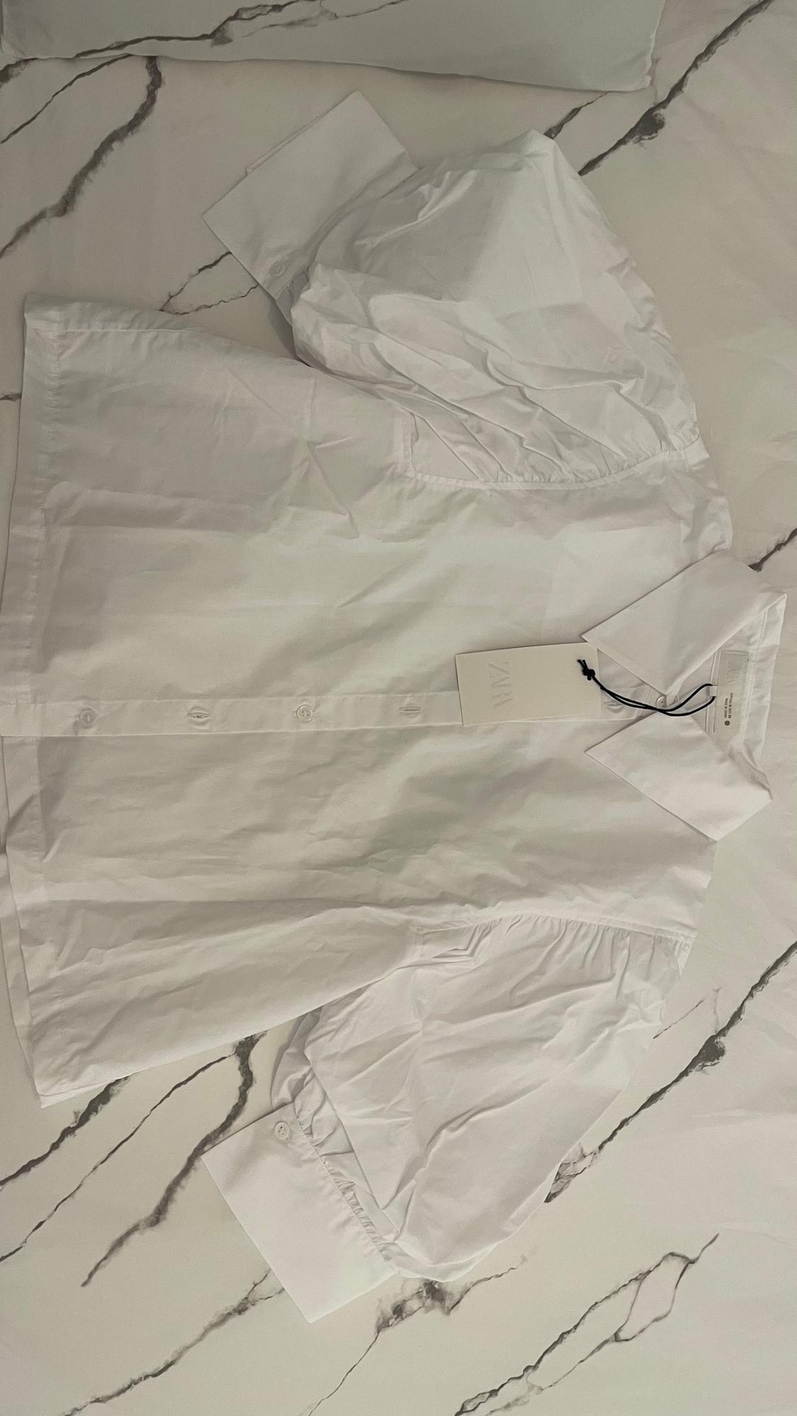 White short-sleeved shirt with label on marble background. The label says "ZARA".
