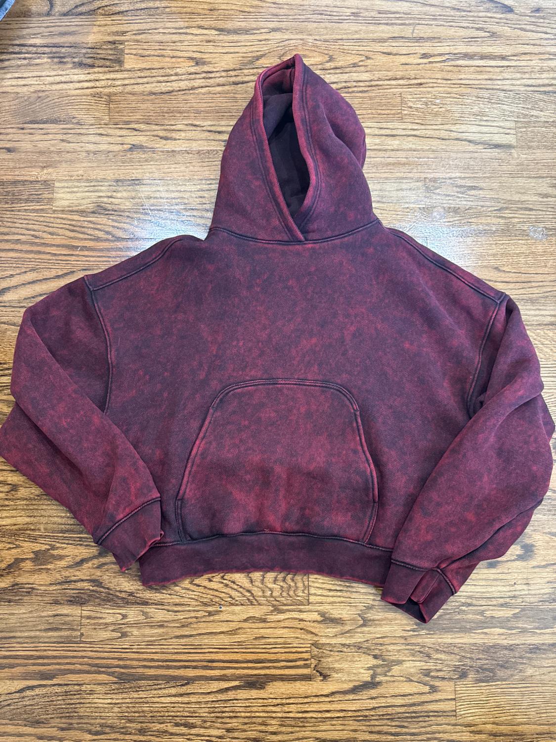 Burgundy and black washed-effect hoodie with a front pocket, laid out on a wooden floor.