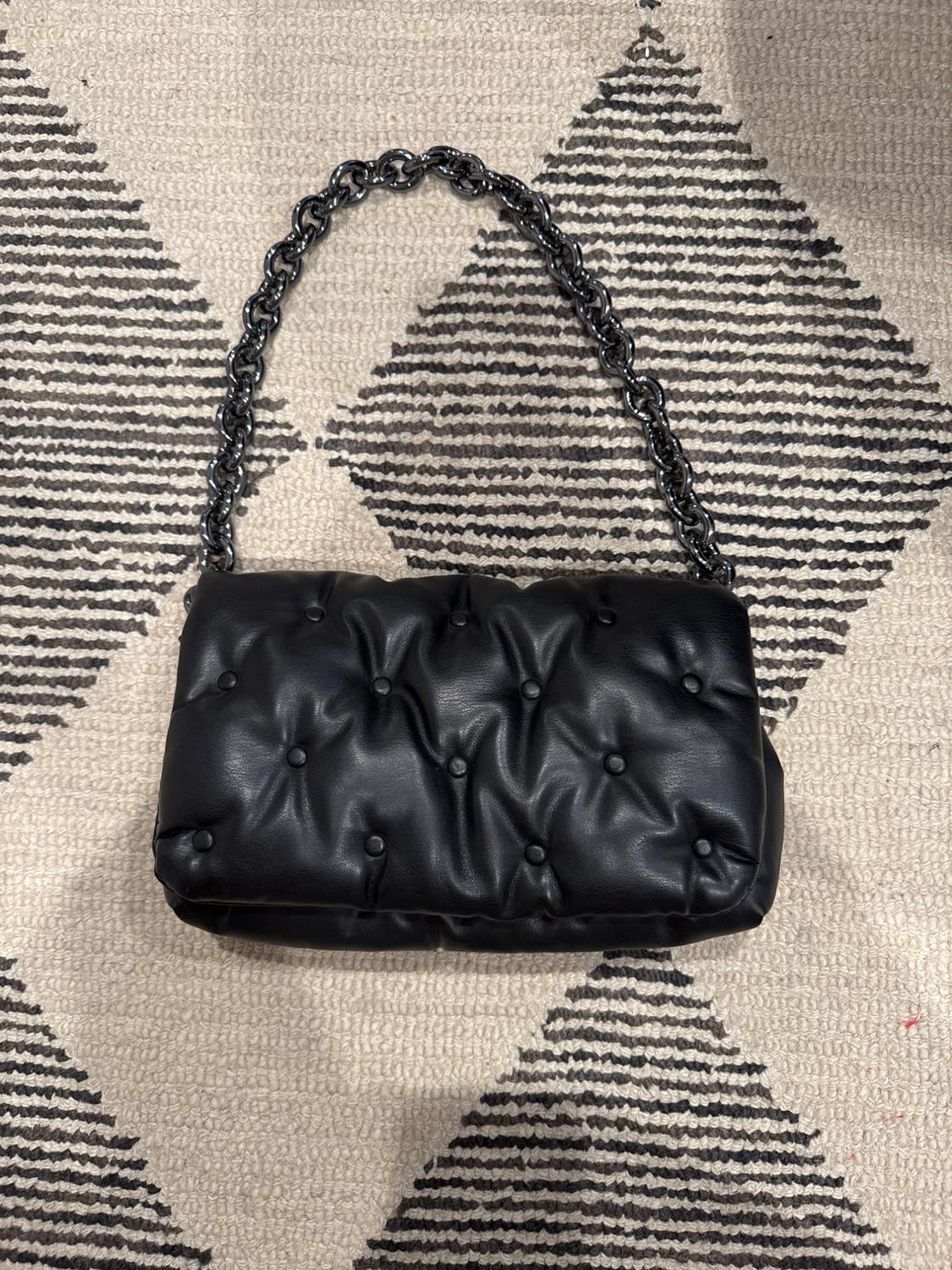 Black quilted handbag with metallic chain on a black and white geometric pattern rug.
