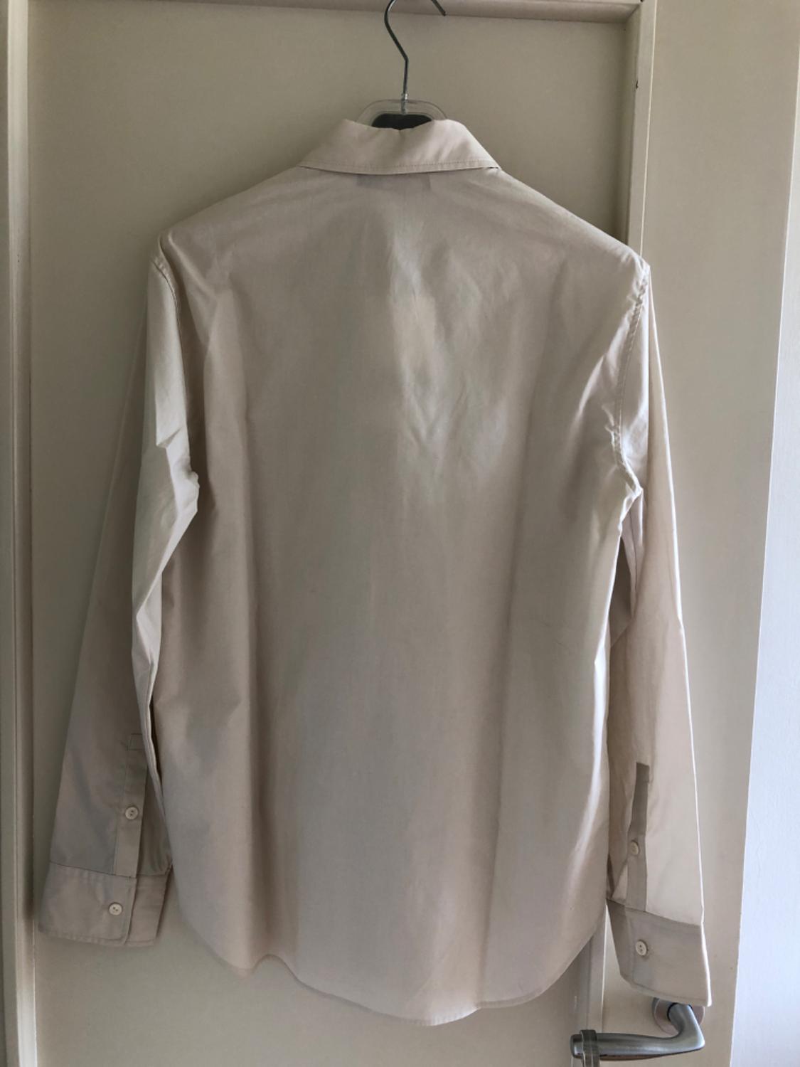 White long-sleeved shirt hanging on a hanger over a white door, viewed from the back.