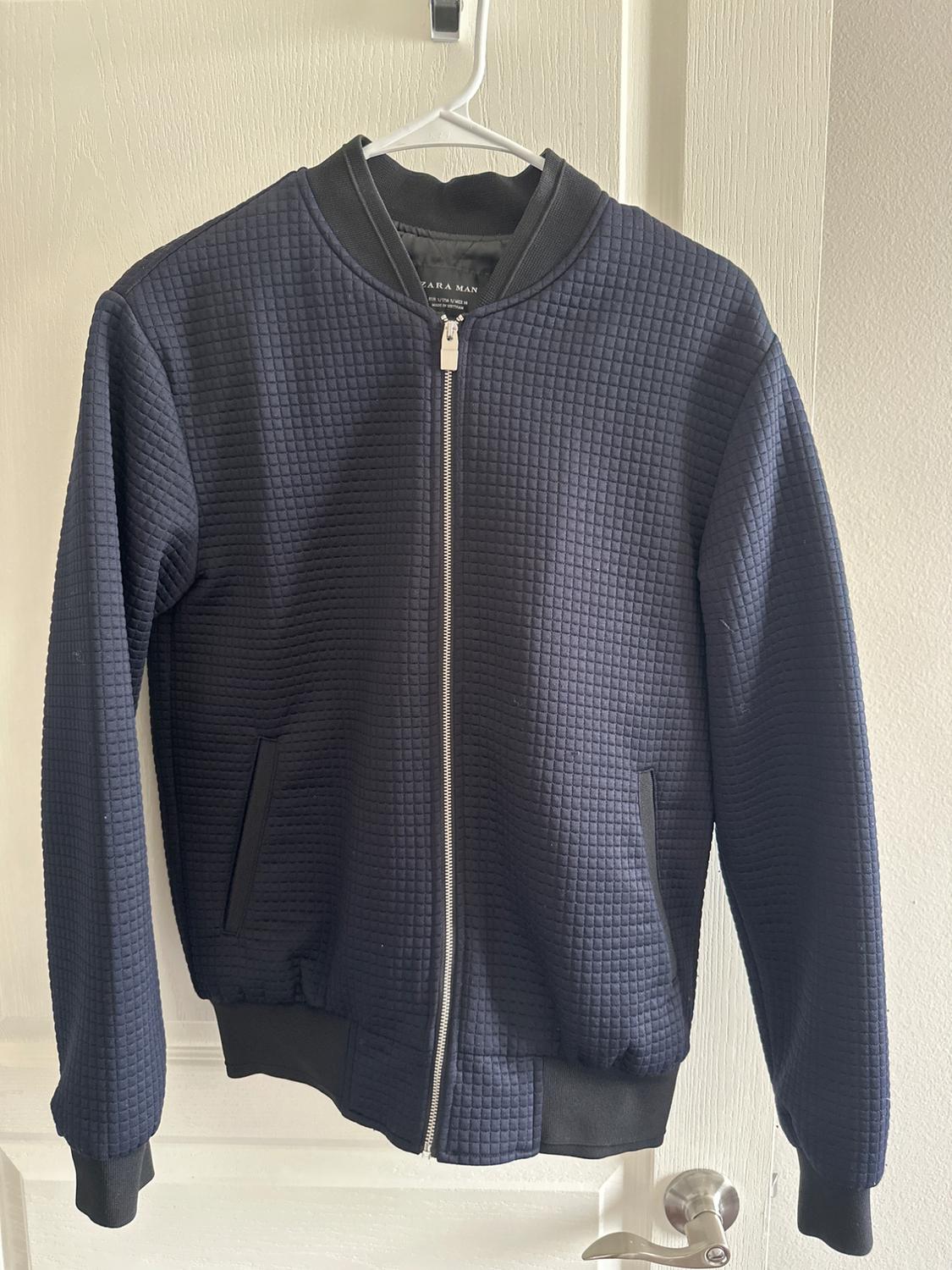 Front view of a navy blue jacket with a square texture and a front zip fastening.