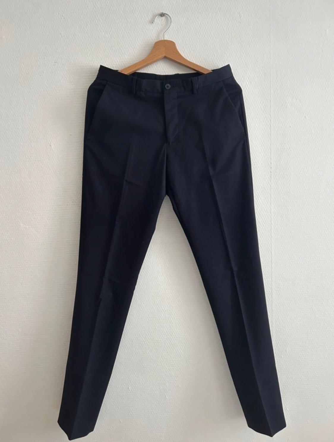 Black trousers hanging on a wooden hanger against a white wall.