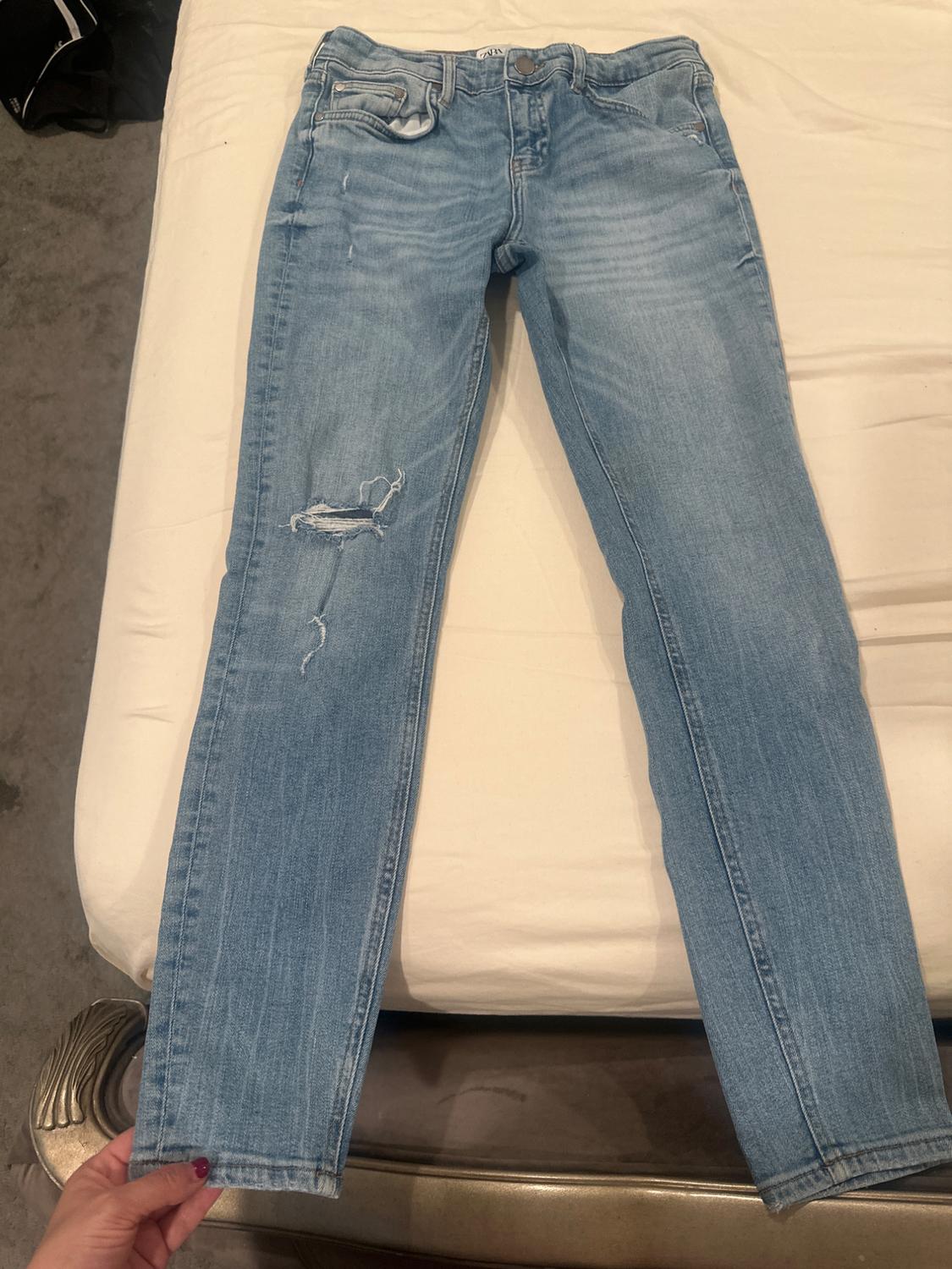 Front view of blue denim jeans with rips and front pockets.