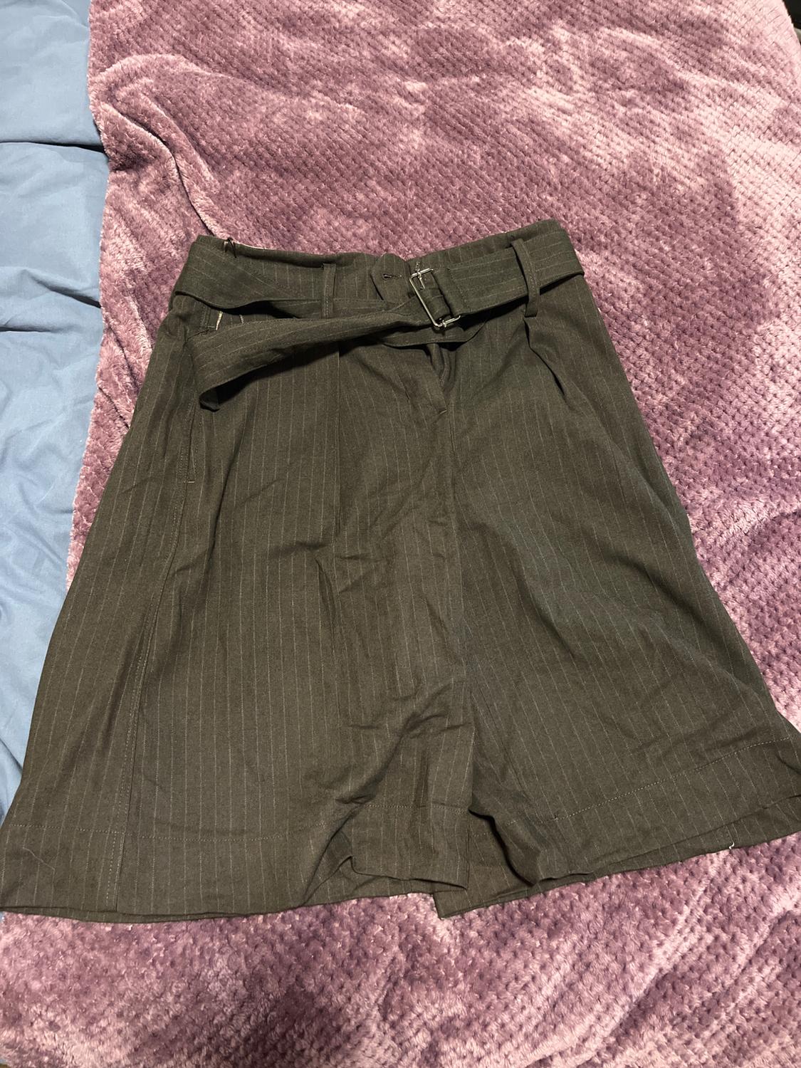 Dark fabric shorts with a belt, on a soft-textured lilac blanket and a light blue background.