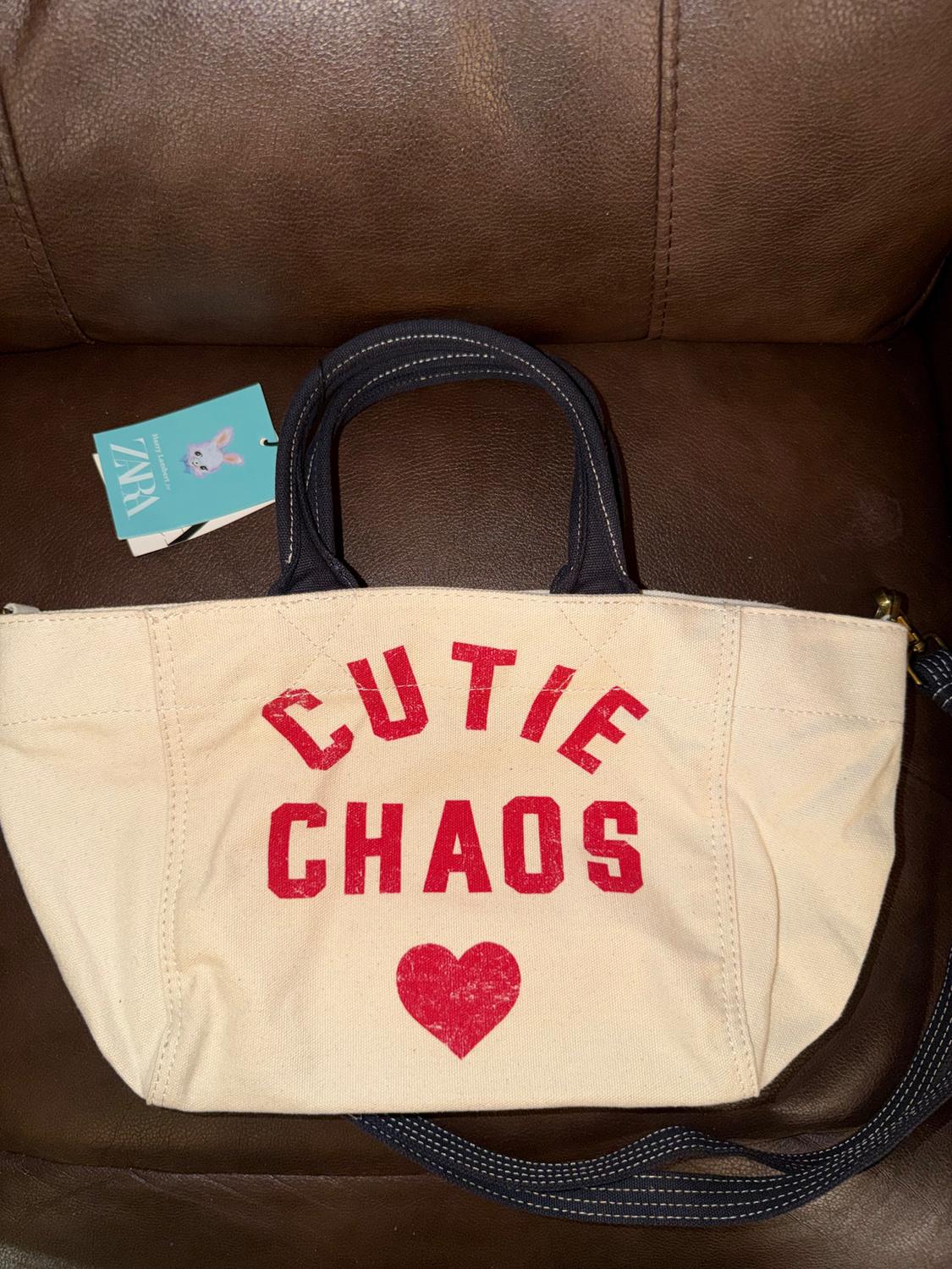 Beige fabric bag with black handles on a brown sofa. Red text "CUTIE CHAOS" and a heart. Blue tag with a rabbit.