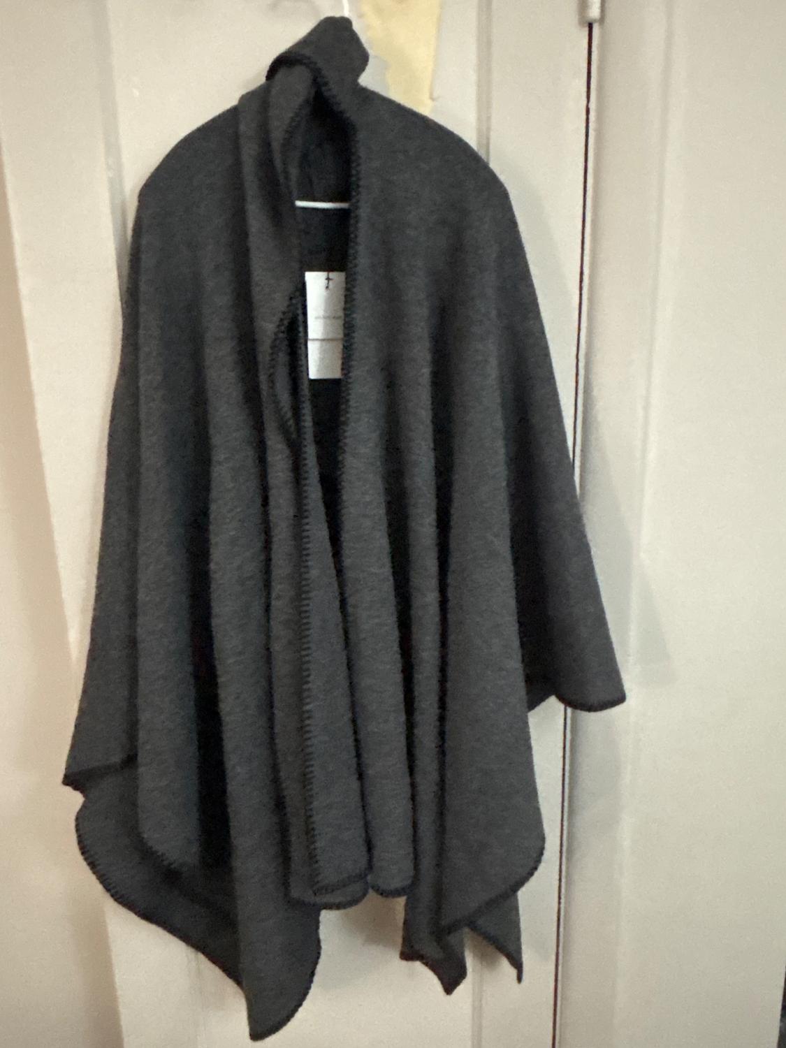 Dark grey poncho with a hood and sewn trim, hanging on a white door with a visible label on the inside.