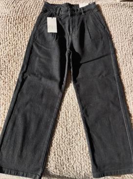 Black wide-leg trousers on a textured surface, with a white tag hanging from the waistband.