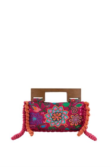 Front view of a fuchsia handbag with colorful floral embroidery, a wooden handle, and a snap button closure.