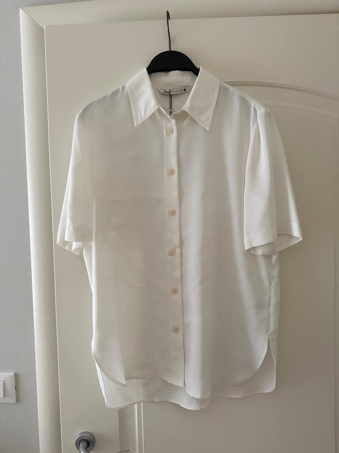 White short-sleeved shirt hanging on a black hanger over a white door.