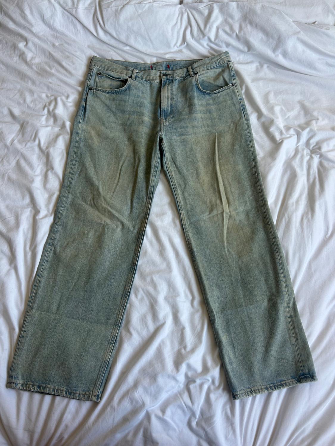 Light blue denim jeans placed on a bed with wrinkled white sheets.