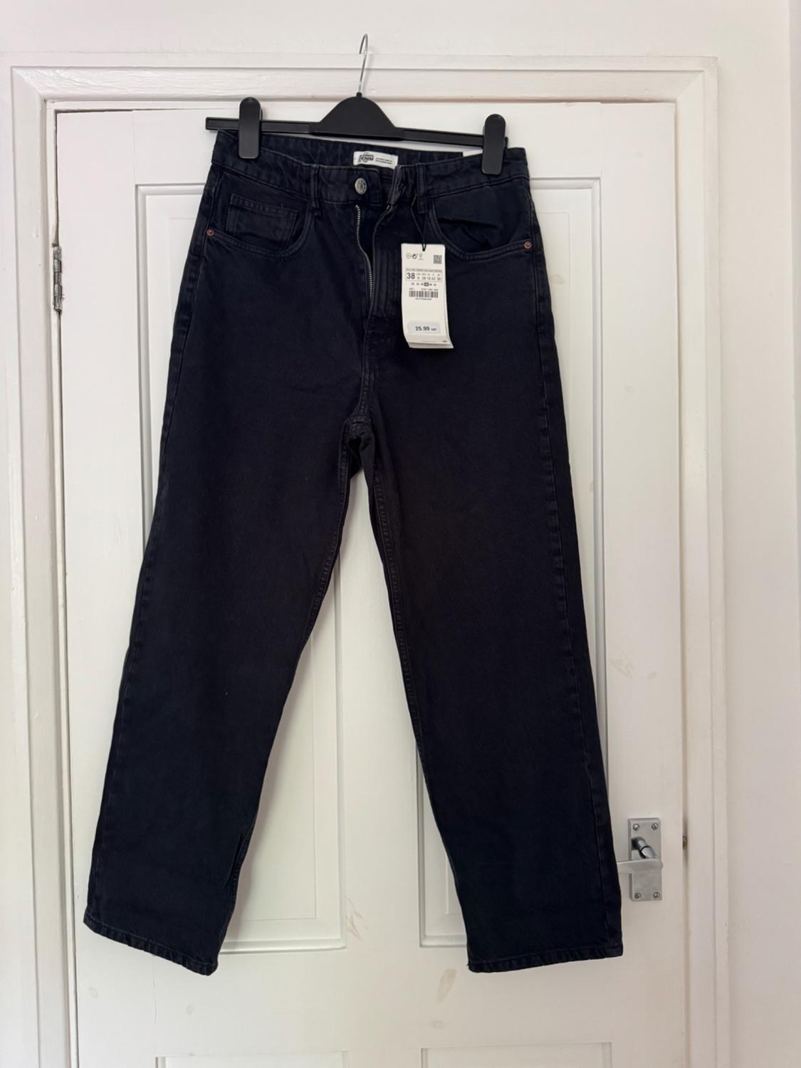 Black jeans on a hanger over a white door. Casual style, zip slightly open and visible tag with the number 38.