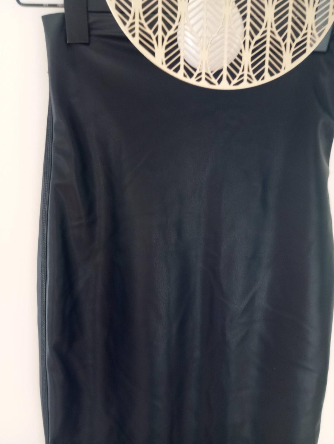 Black skirt made of smooth material, hanging on a hanger with a decorative leaf design at the top.