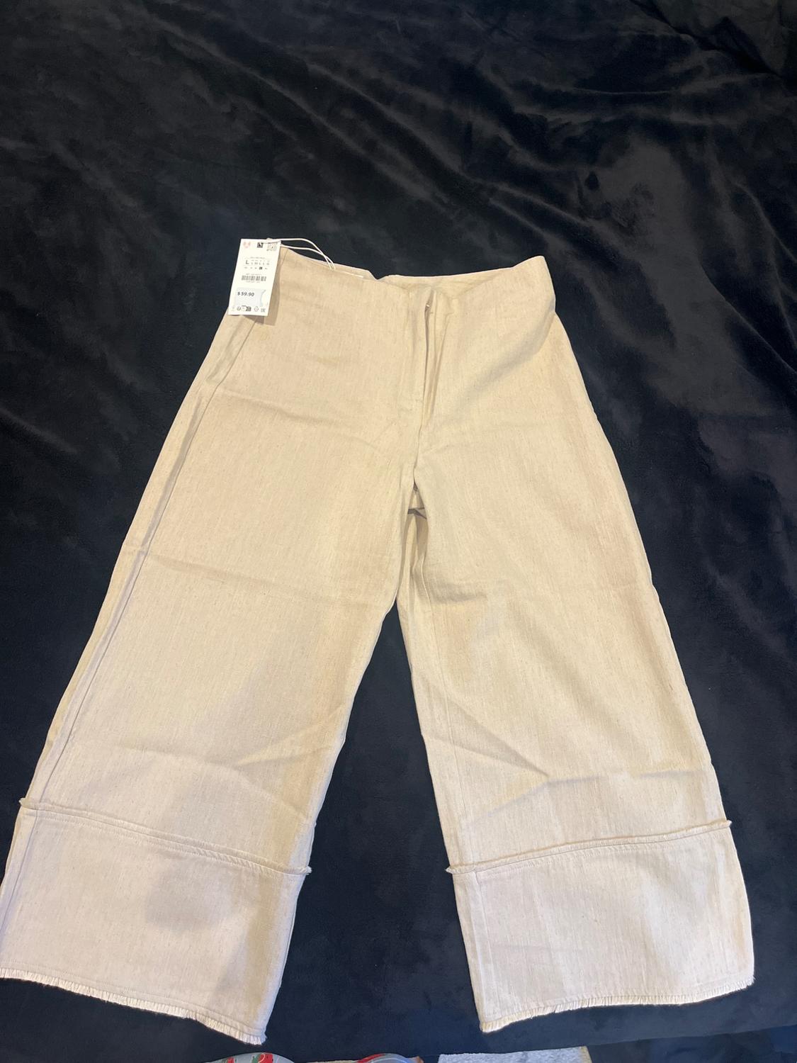 Beige wide-leg trousers on a black background, with a visible label on the waistband.