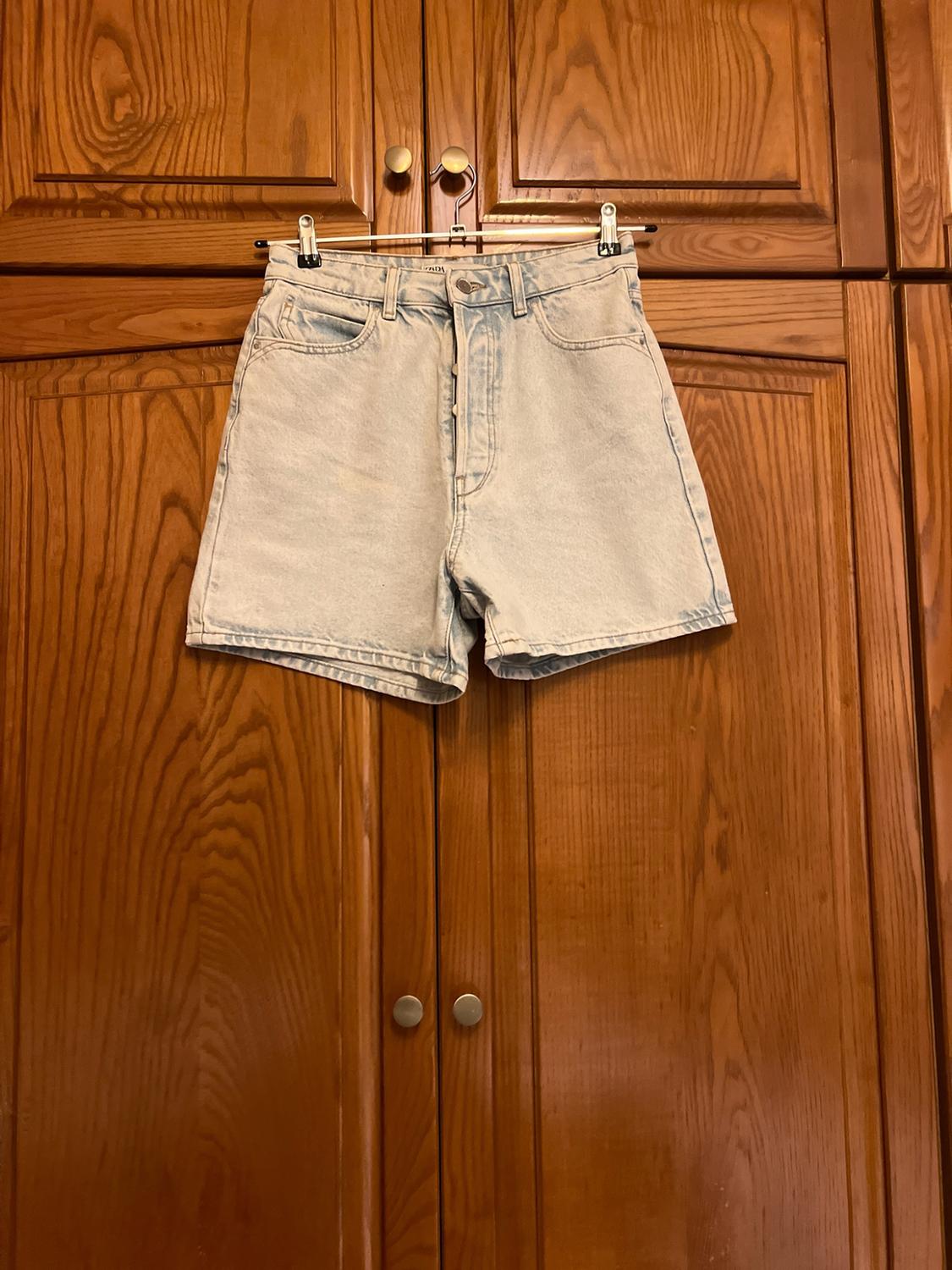 Light blue denim shorts hanging from a hanger in a wooden wardrobe. Casual and relaxed style in a homely setting.
