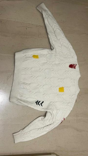 White cable knit jumper with yellow, red and black patches on a light wooden floor.