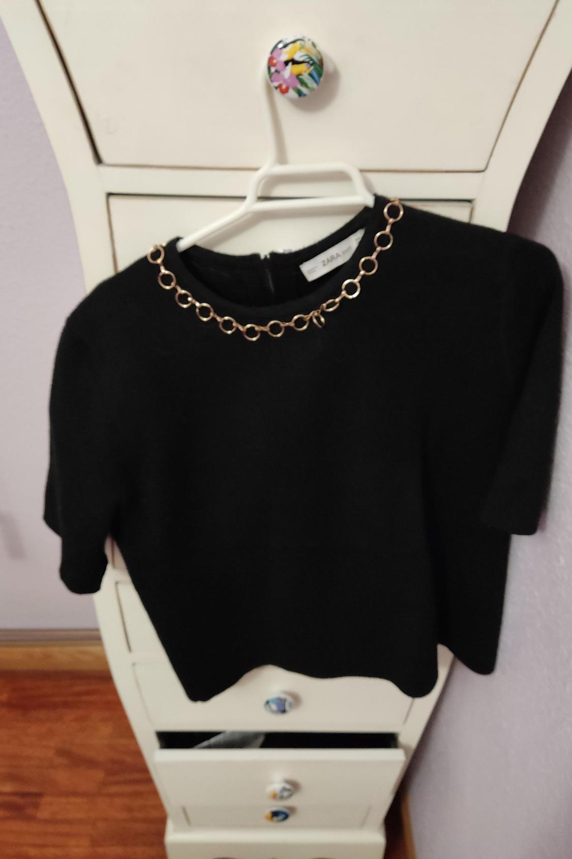 Front view of a black blouse with a gold chain at the neck.
