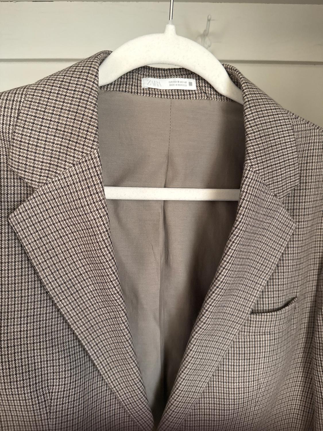 Brown and white checkered jacket on a white hanger. Visible tag: "ZARA, MADE IN MOROCCO". White background.