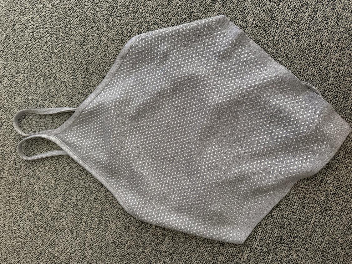 Grey top with thin straps and a small white polka dot print on a textured grey background.
