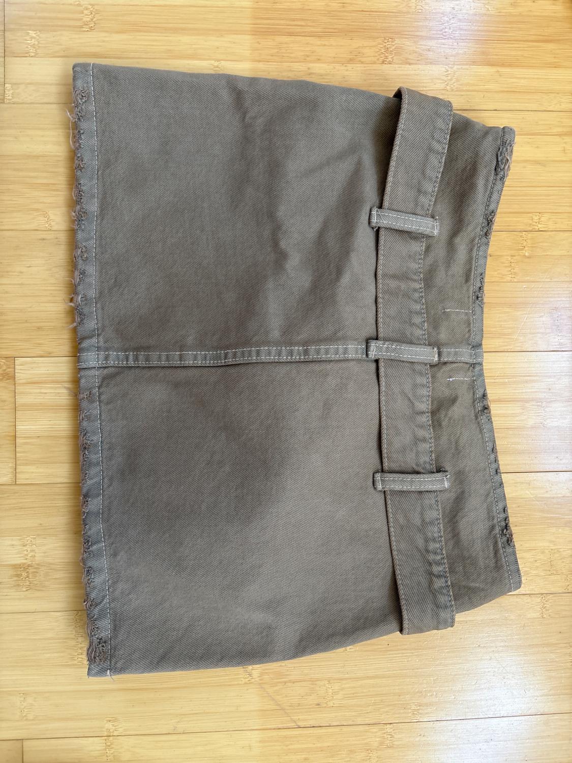 Brown short skirt on light wood flooring, with a waistband and frayed details on the bottom left edge.