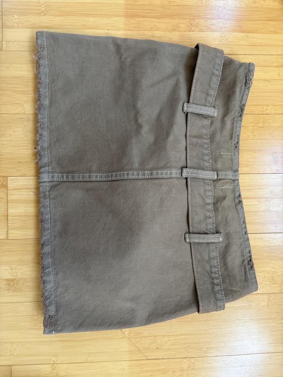 Brown short skirt on light wood flooring, with a waistband and frayed details on the bottom left edge.