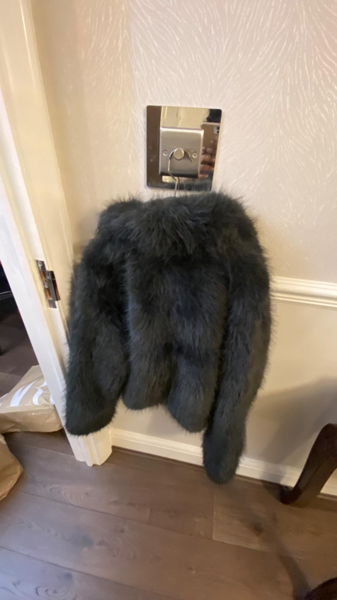 Dark grey faux leather jacket hanging on a metal wall hook, above a light wooden floor.