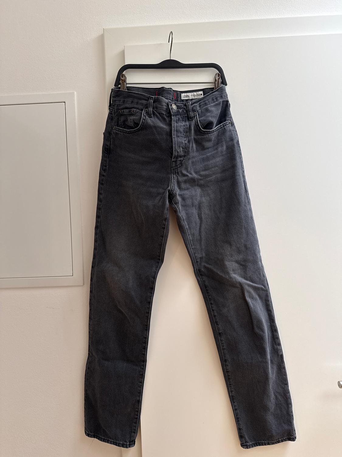 Black jeans hanging on a black hanger over a white door. Label visible on the waistband.