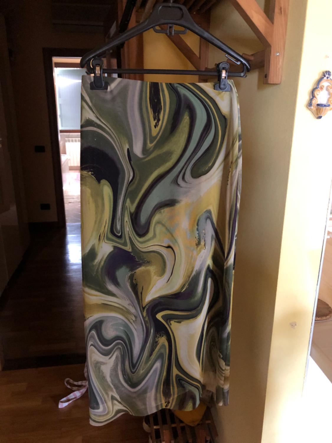 Skirt hanging on a hanger with an abstract print in shades of green, yellow and black, in a dimly lit interior.
