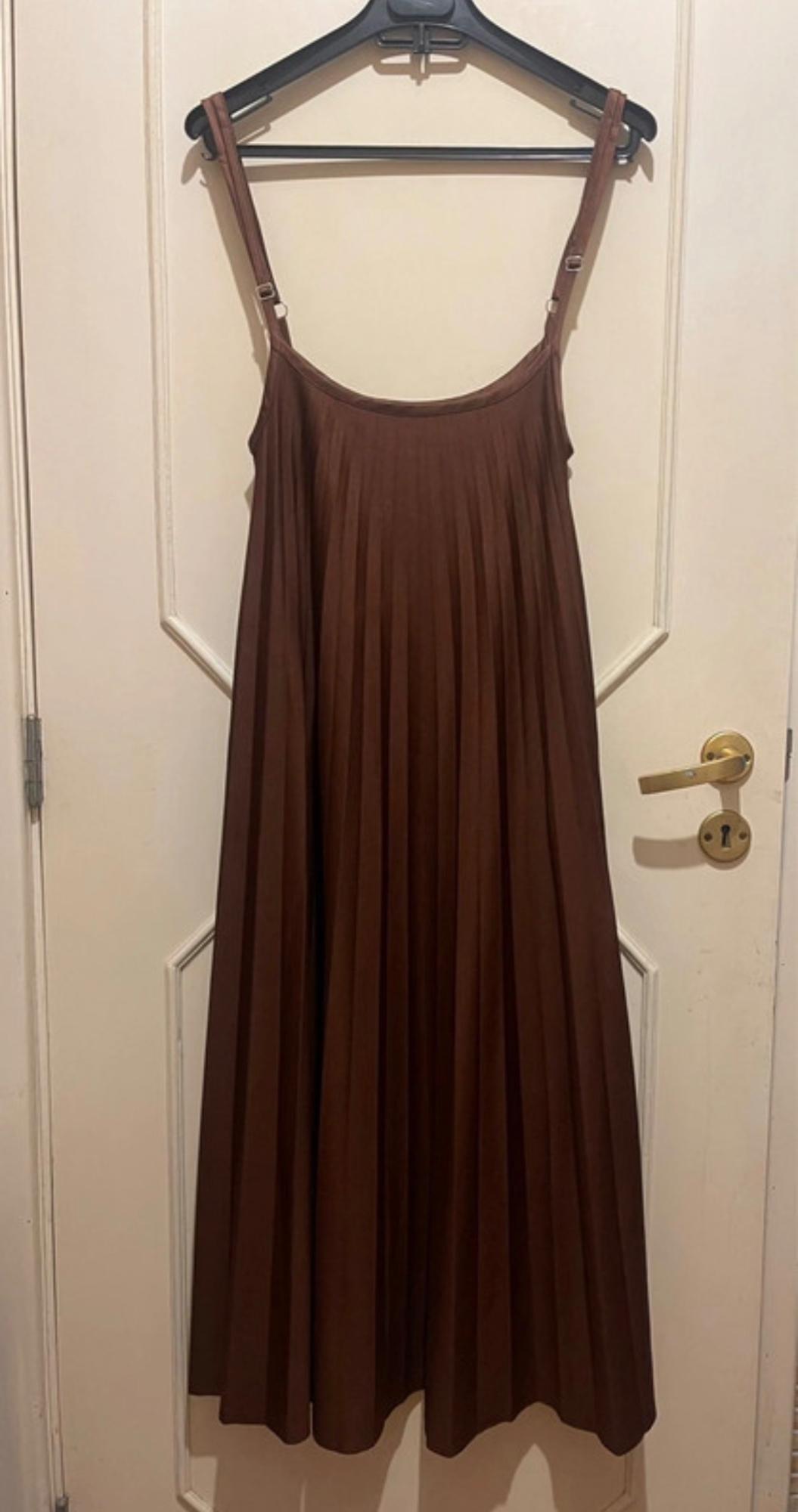 Pleated brown dress with adjustable straps, hanging on a black hanger over a white door with a gold handle.