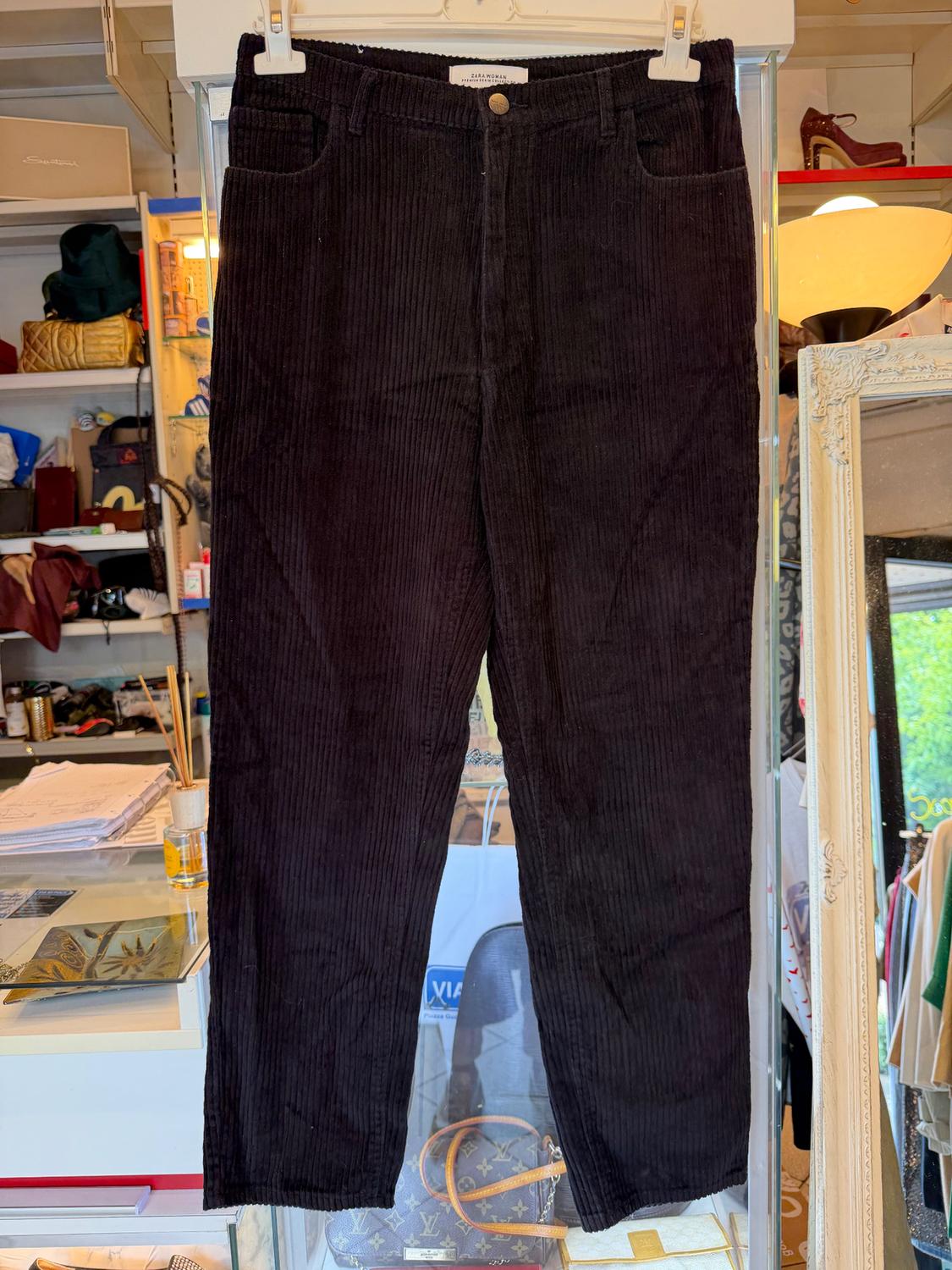 Black corduroy trousers hanging in a shop, with a background of shelves full of accessories and clothes.