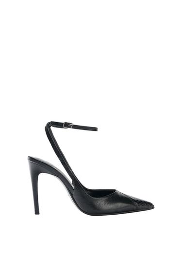 Black high-heeled shoe with a pointed toe and adjustable ankle strap, on a white background.