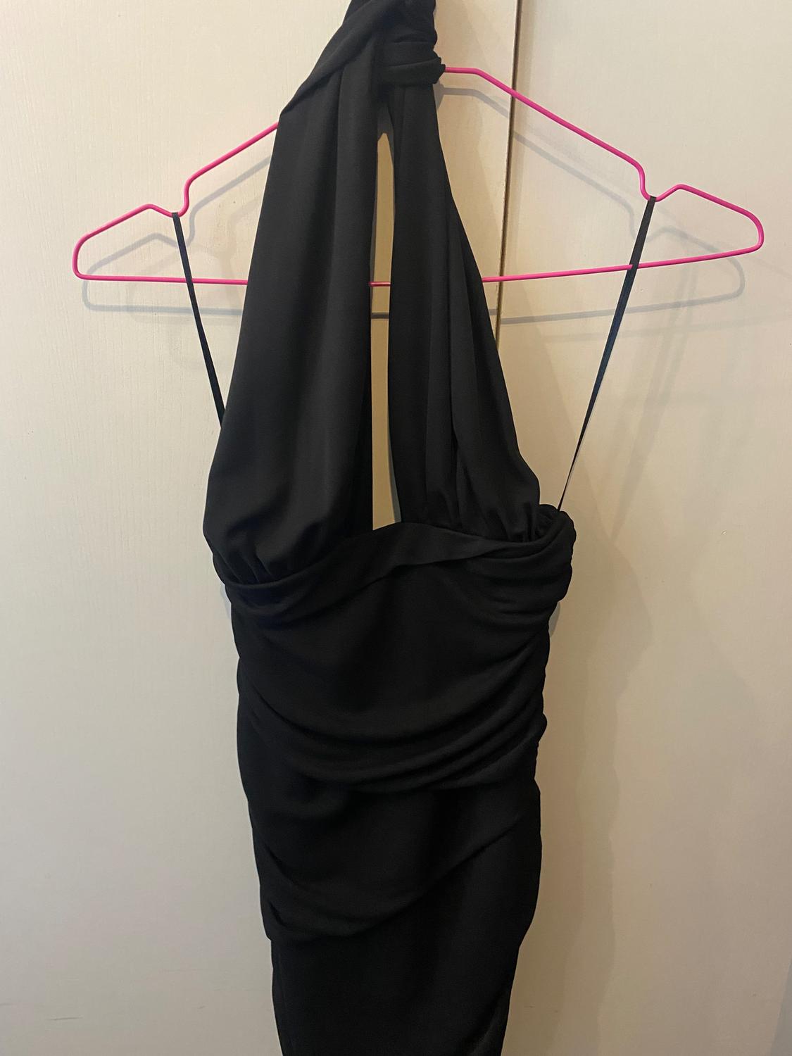 Black draped dress hanging on a pink hanger, white background.