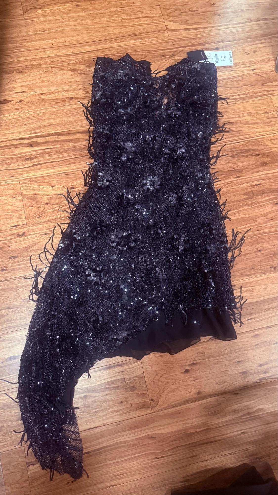 Asymmetric black sequined dress with fringe and tag on a hardwood floor.