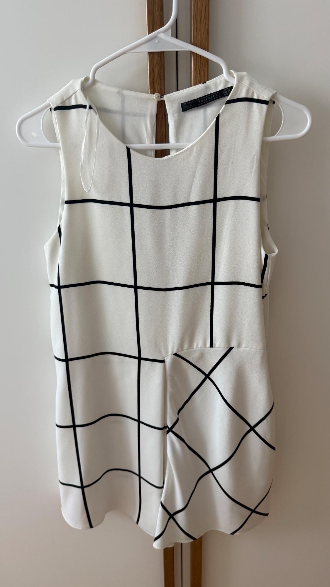 White sleeveless top with black striped pattern and ZARA TRAFALUC label, hanging on a white hanger against a light, wood-panelled background.