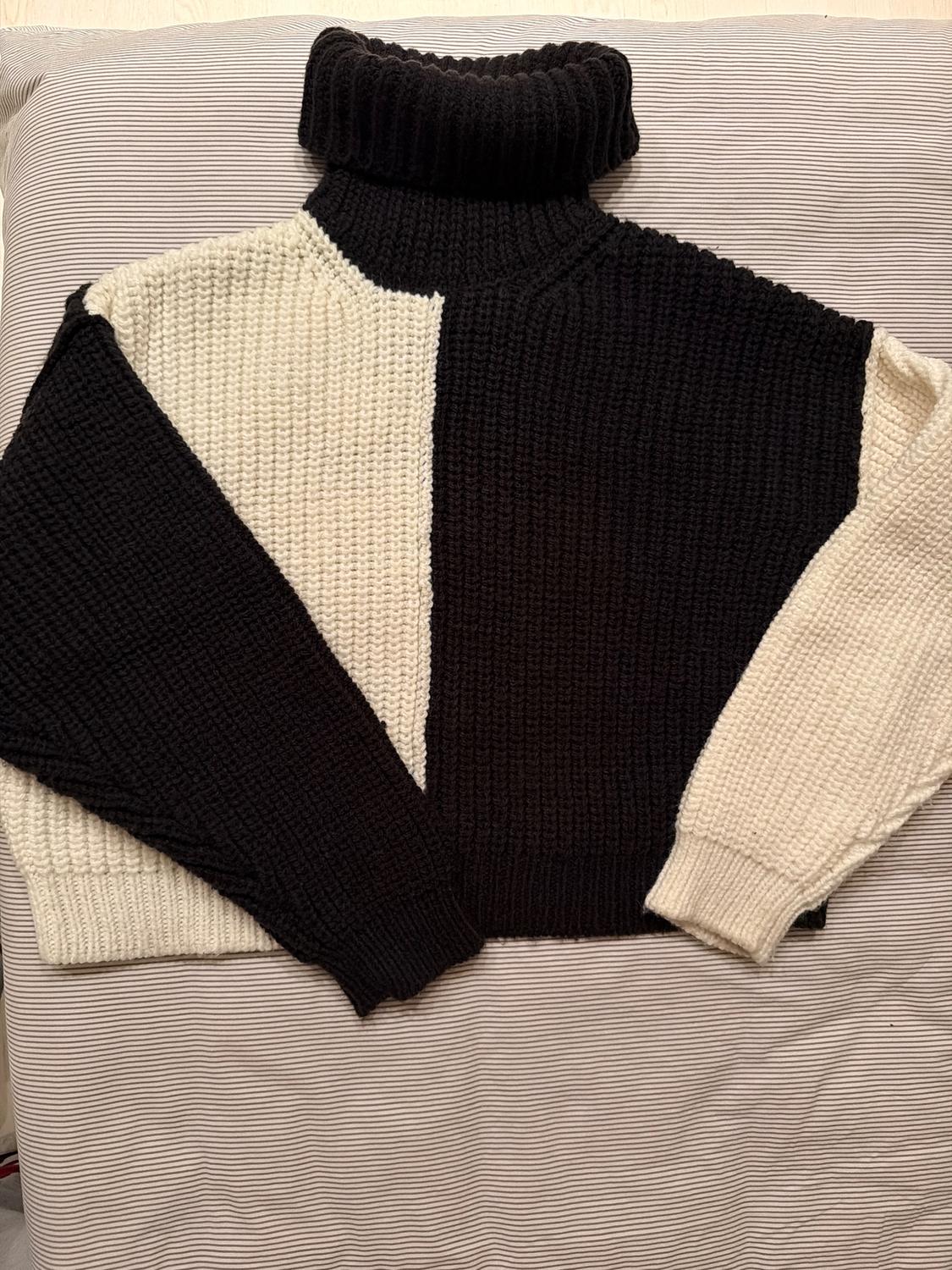 Chunky knit black and white roll-neck jumper, placed on a striped fabric surface.