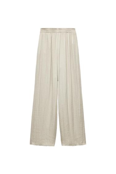 Light beige wide-leg fluid trousers with an elasticated waist and textured fabric, presented against a white background.