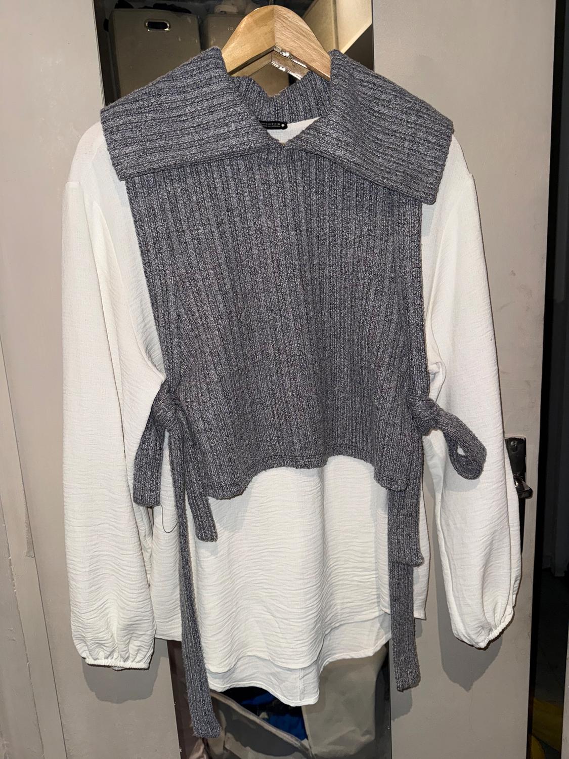 White blouse with a grey ribbed knit waistcoat, hanging on a wooden hanger in a wardrobe.