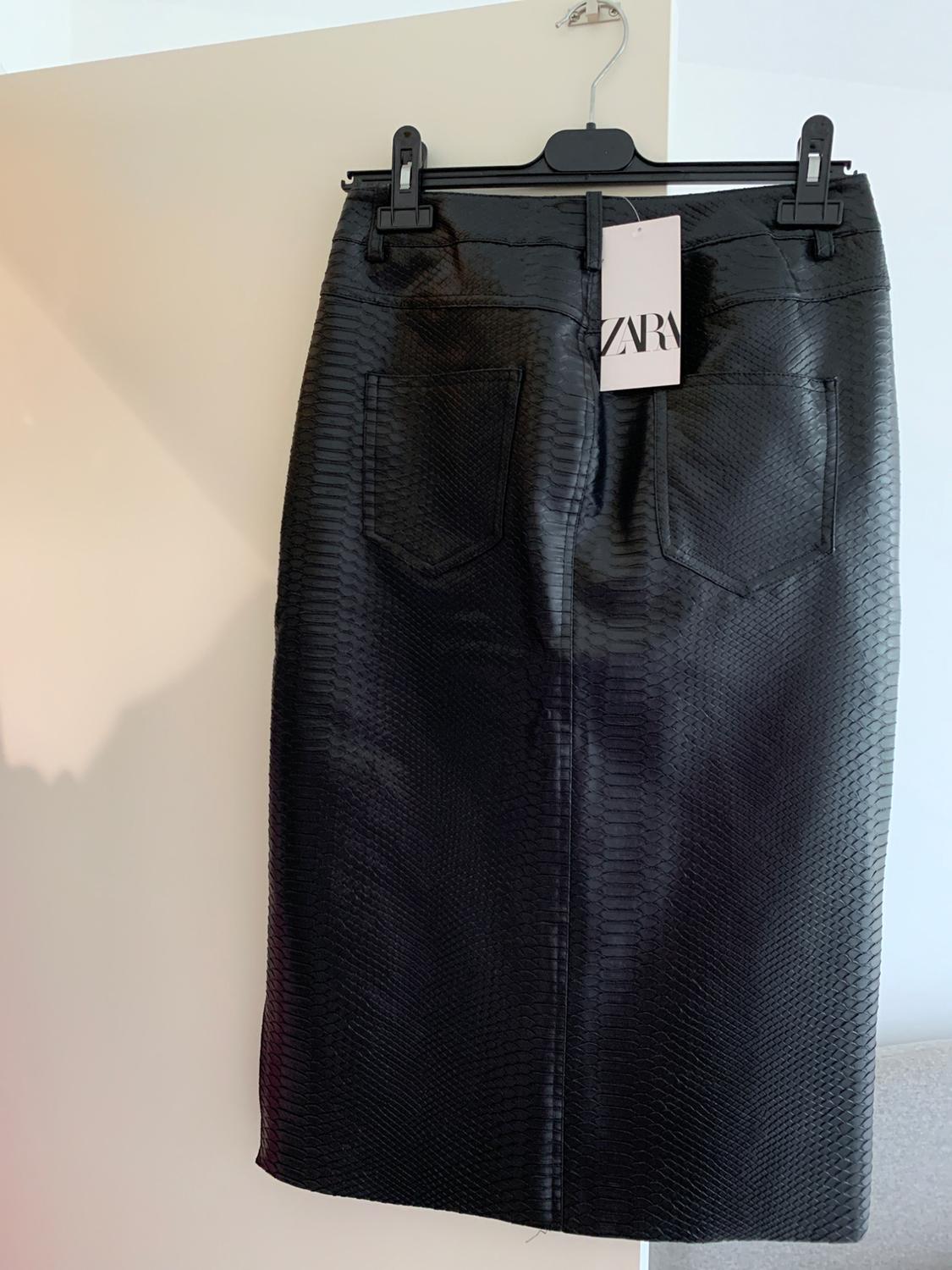 Black snake-skin textured skirt hanging on a clothes hanger. Visible label with the text "ZARA". Light background.