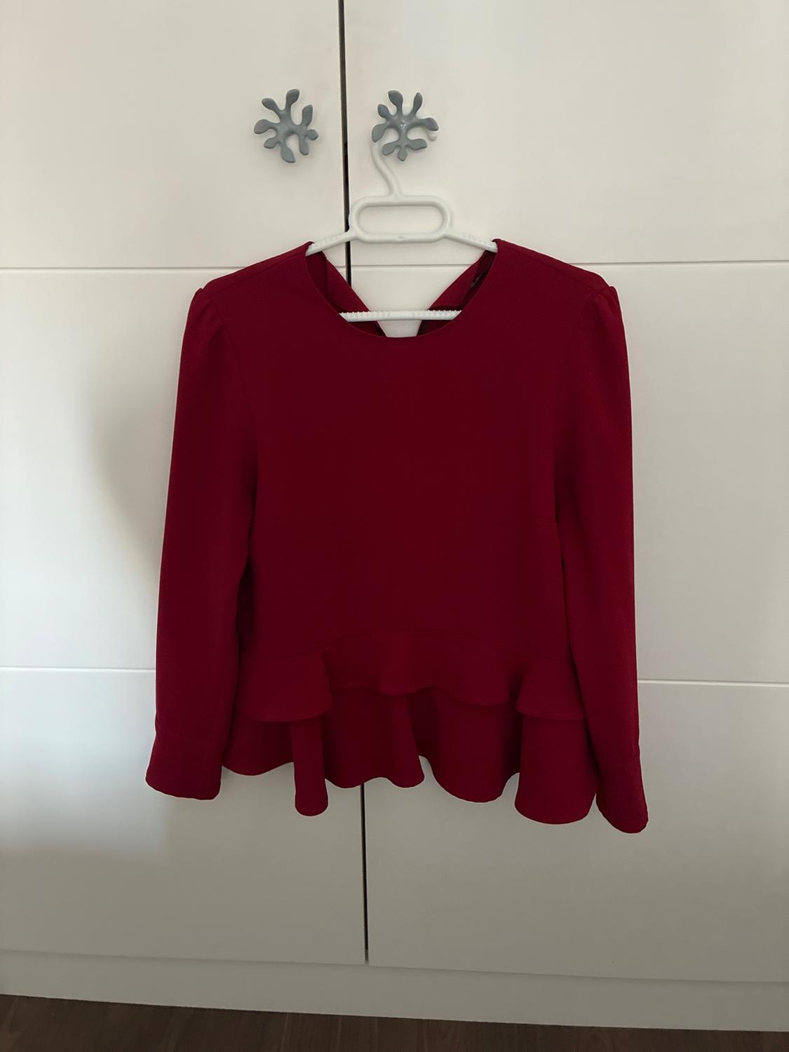 Red long-sleeved blouse with a ruffled hem, hanging on a hanger from the star-shaped handle of a white wardrobe.