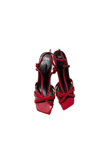 Red heeled sandals with crossed straps and a square toe. Visible text: "ZARA 39". White background.