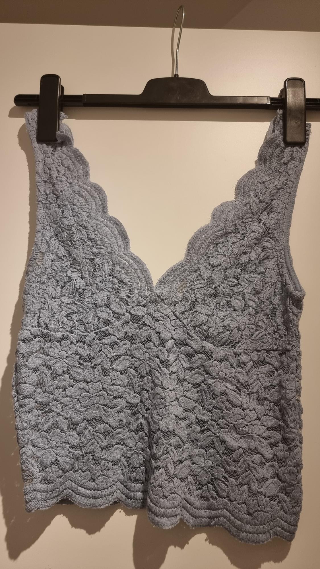 Grey lace top with a V-neck and scalloped edges, hanging on a black hanger against a white background.
