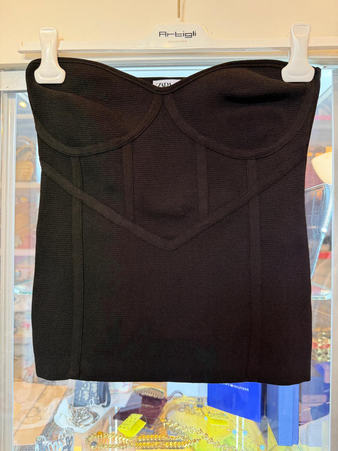 Black strapless top hanging on a white hanger from the Artigli collection, with a background of colourful jewellery and accessories.