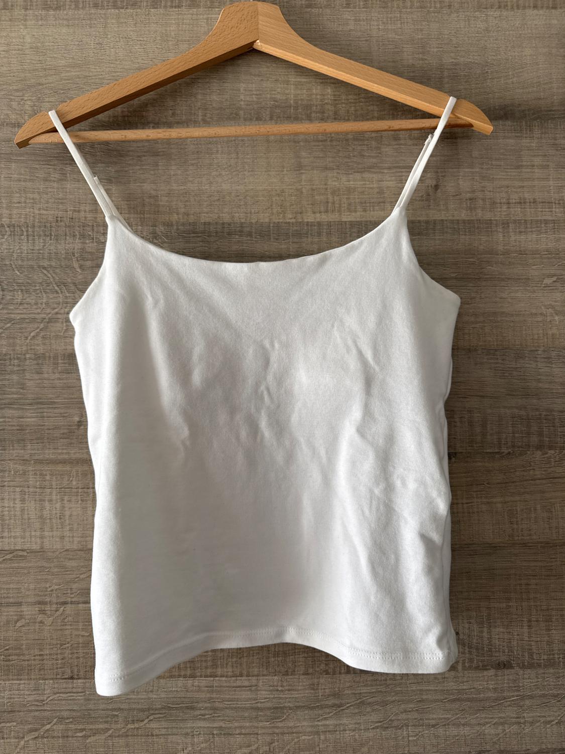 White vest top with thin straps, hanging on a wooden hanger against a light wooden background.