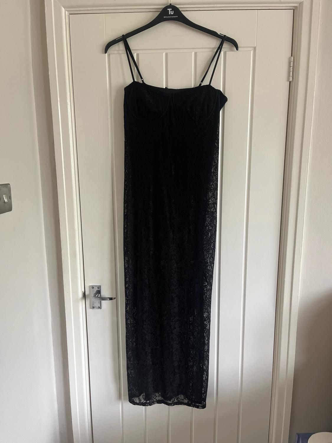 Black lace maxi dress with spaghetti straps hanging on a hanger with the text "Tu" over a white door.