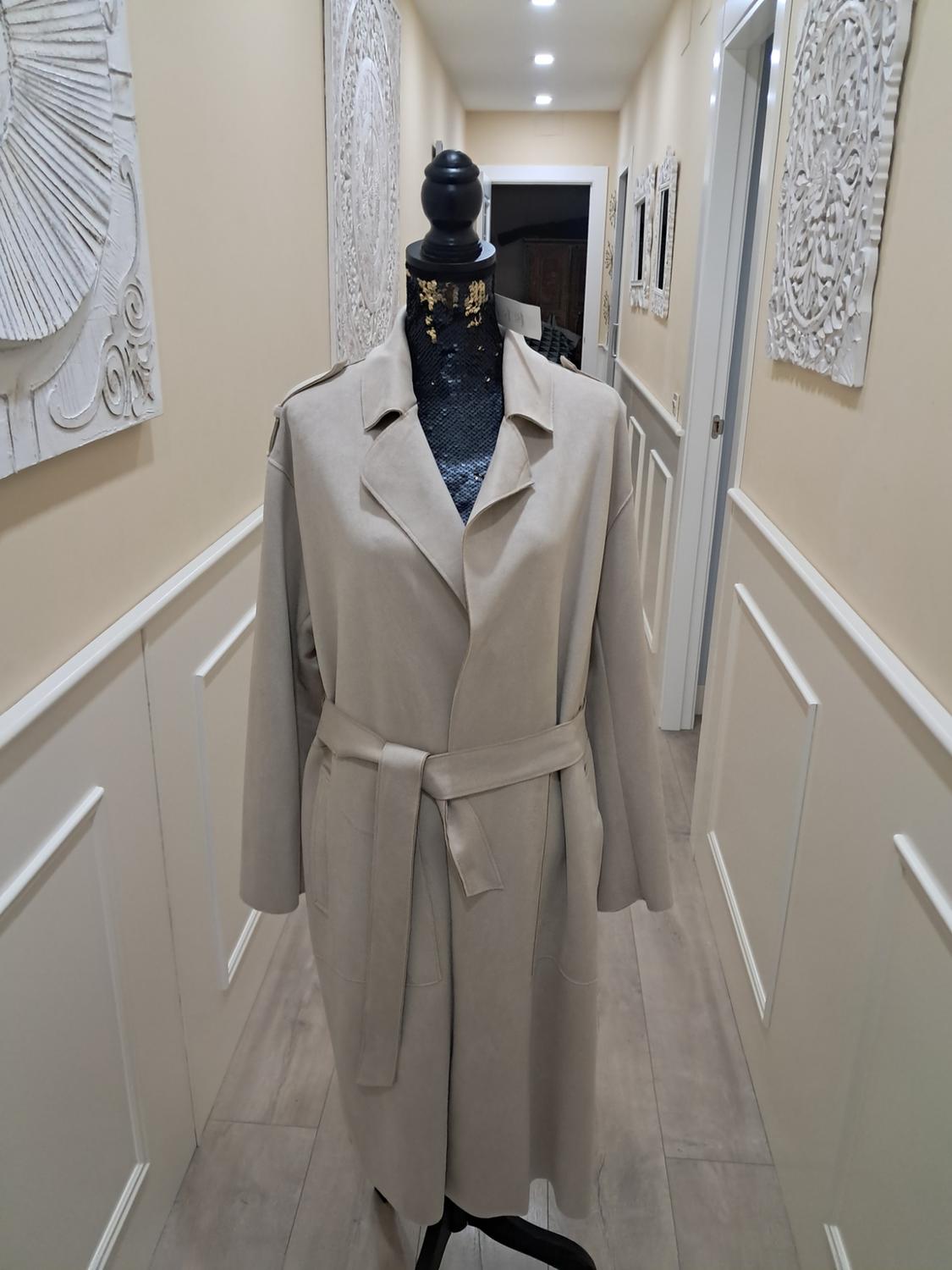 Mannequin in a belted beige coat in a hallway decorated with white panelling and embossed art on the walls.