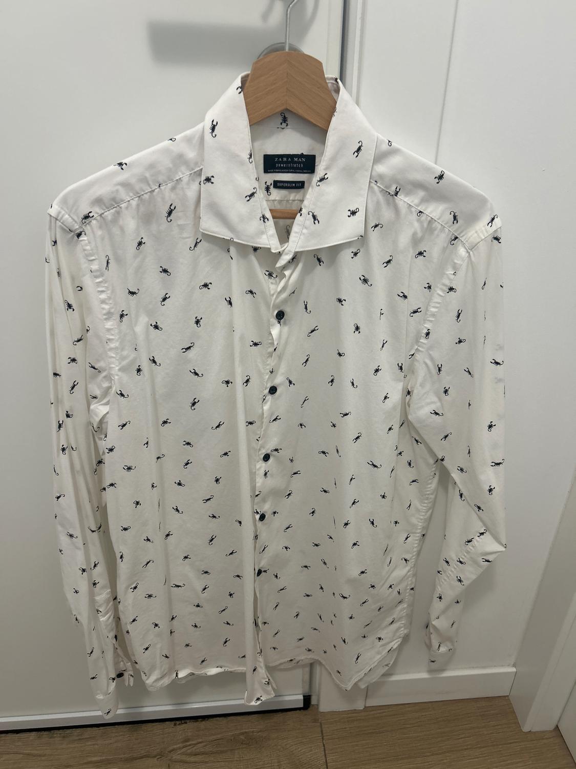 White shirt with a small black scorpion print, hanging on a wooden hanger over a white door.