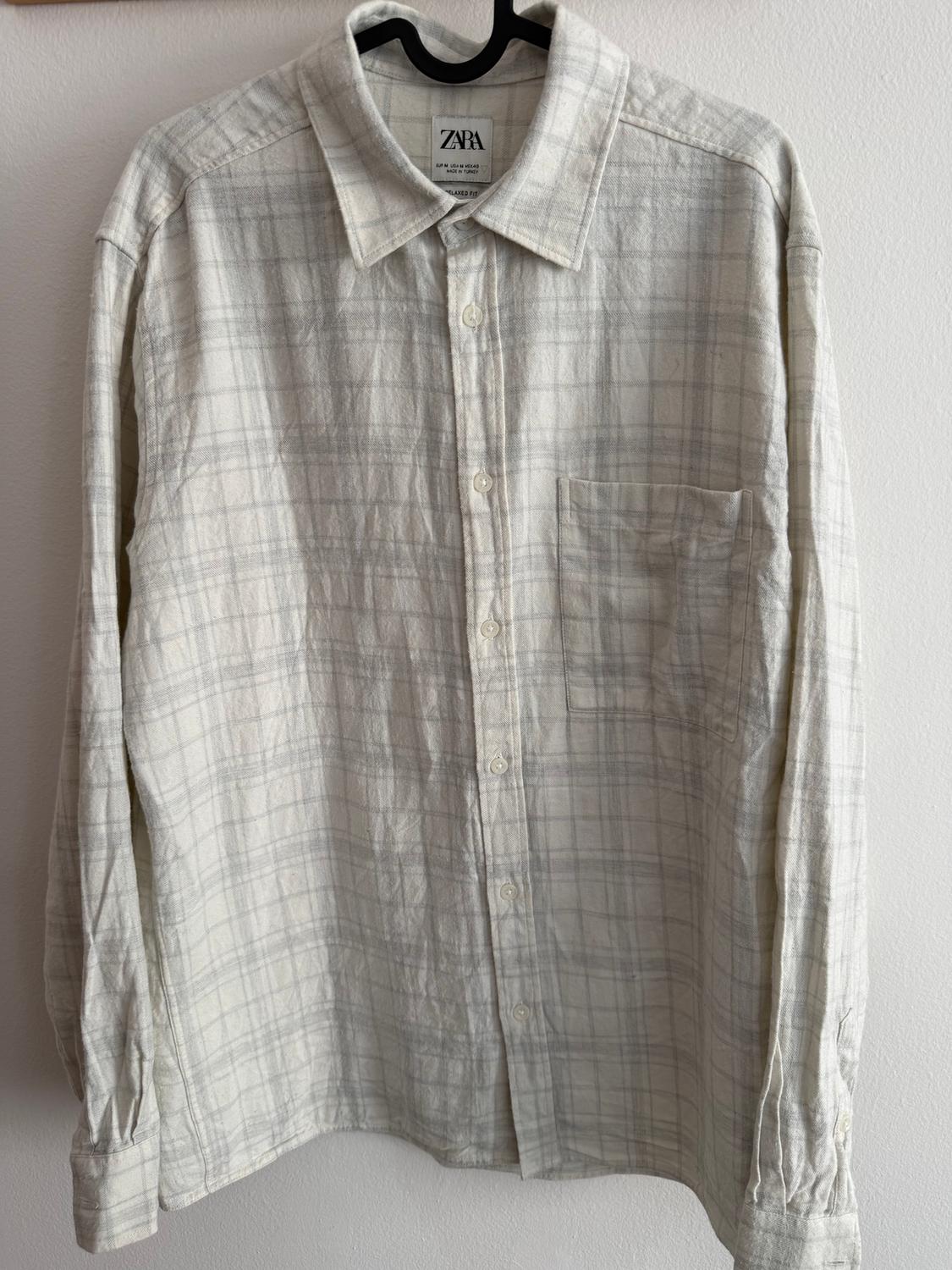 Light-coloured checked shirt hanging on a black hanger. Visible label with the text "ZARA". White background.