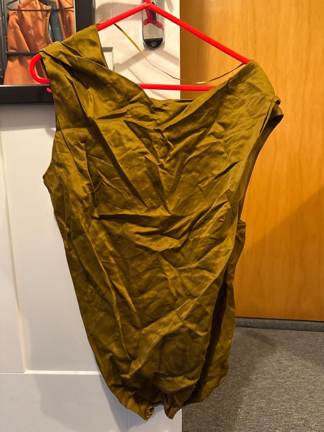 A creased mustard-coloured dress hanging on a red hanger above a wooden door. A reflection of clothing in the mirror in the background.