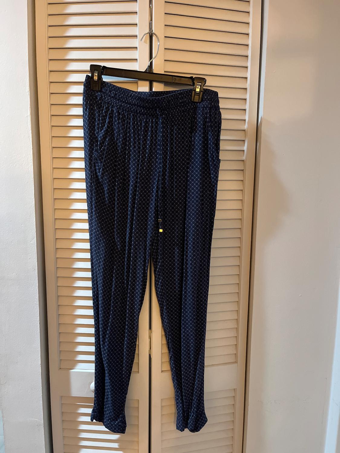 Dark blue trousers with a white polka dot pattern hanging on a black hanger in front of a white roller shutter door.
