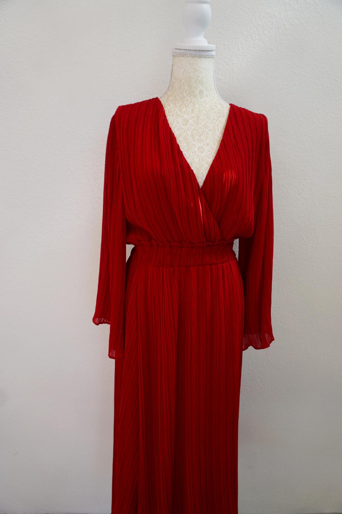 Long red pleated dress with an elasticated waist, V-neck, and long sleeves, on a mannequin with lace in front of a white background.