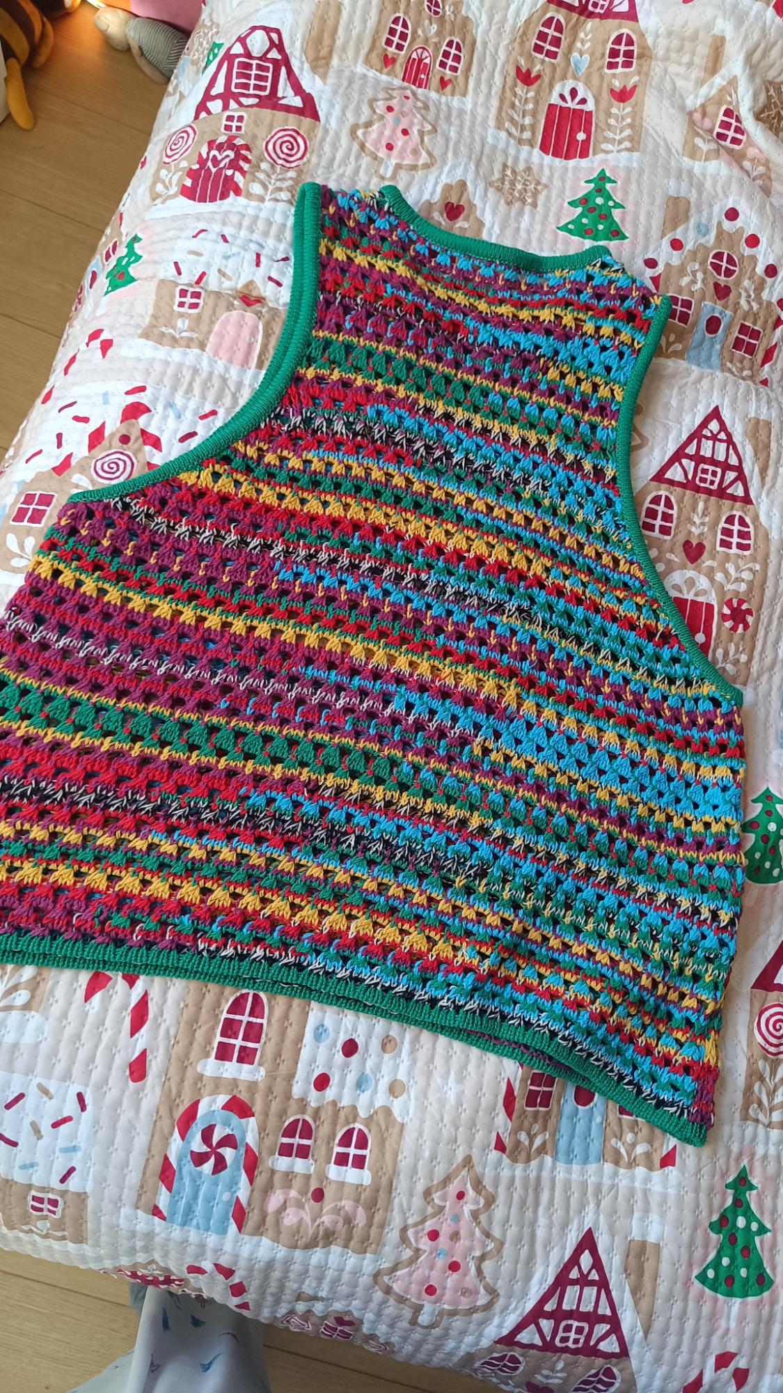 Multicoloured crochet waistcoat on a quilt with a Christmas gingerbread house and tree print.